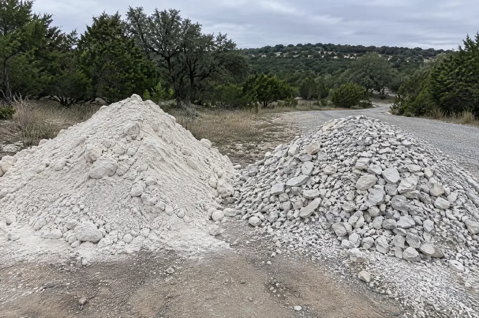 Caliche vs crushed limestone: pile of white caliche next to a pile of gray crushed limestone road base