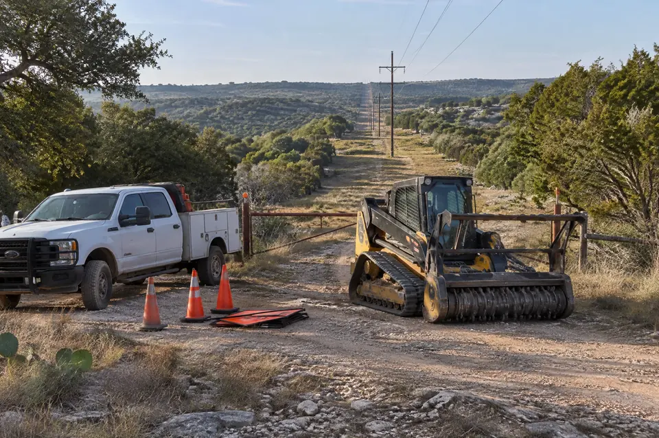 Electrical row safety training: crew truck, safety cones and a forestry mulcher staged at a power line right-of-way gate