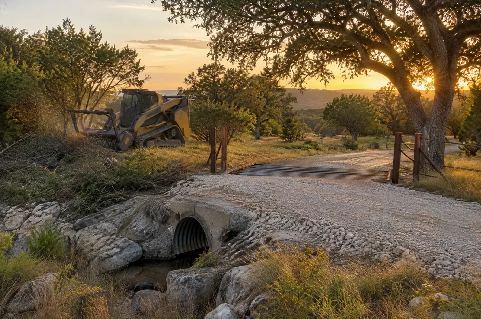 Driveway construction: crowned caliche ranch driveway over a culvert, live oaks alongside
