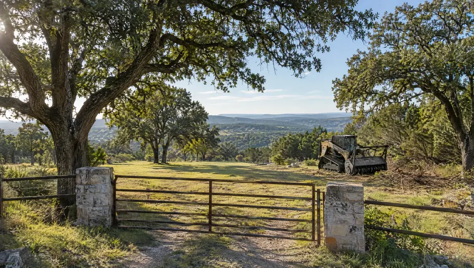 Does clearing land increase property value: park-like Hill Country property with open grass under big live oaks behind a ranch gate