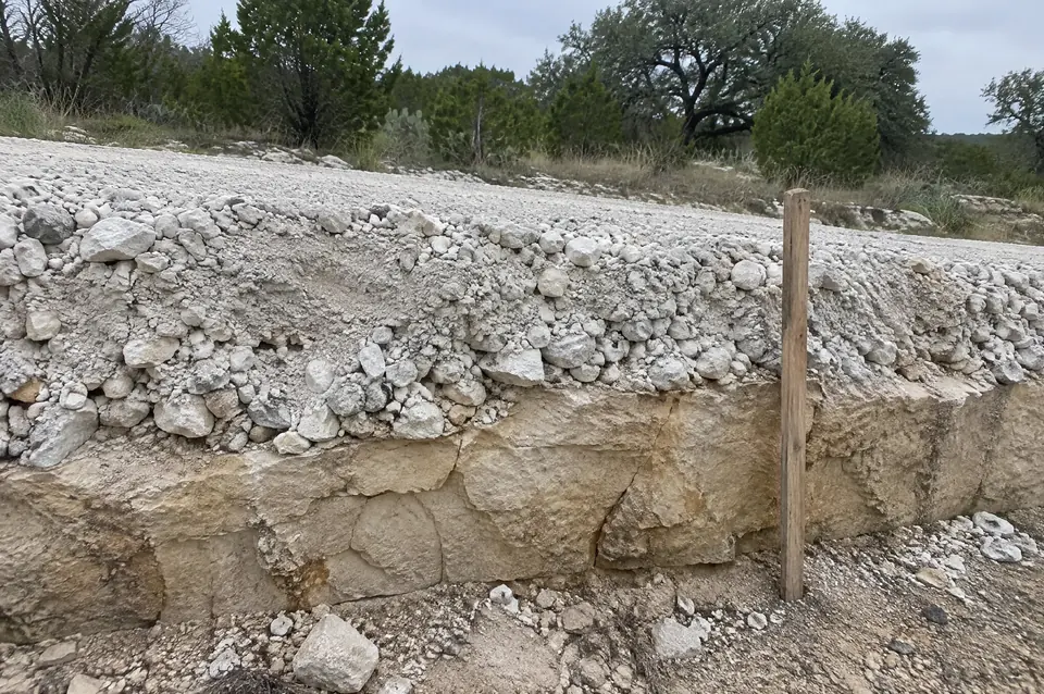 Deep rock crushing: edge of a crushed road bed showing a thick layer of broken limestone over solid ledge