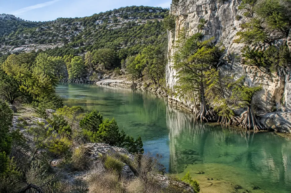 Guadalupe River bend under a tall limestone bluff with bald cypress at the waterline
