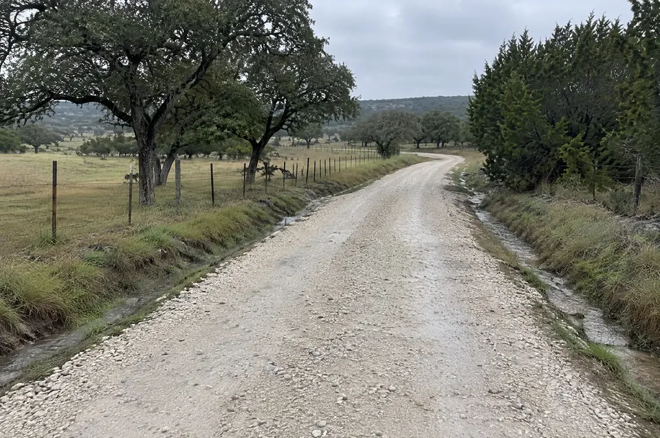 How long does a gravel road last: crowned crushed limestone ranch road draining into a grassy ditch after rain