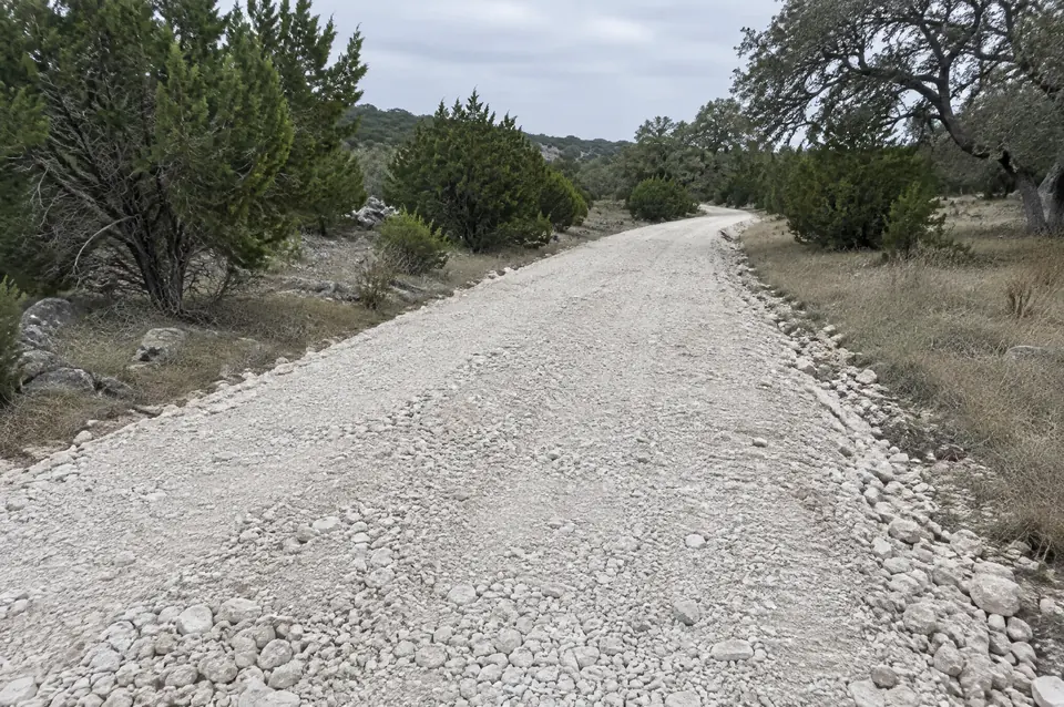 Rock crushing vs hauling road base: limestone crushed in place along a ranch road route, ready to shape and compact