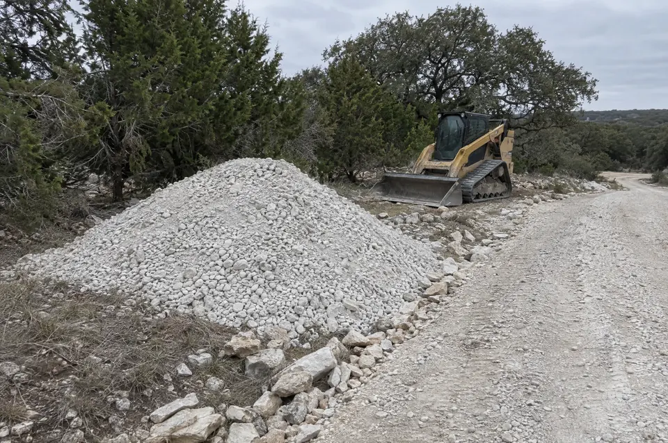 Rock crushing and rock milling in Central Texas: pile of crushed white limestone road base beside a ranch road, track loader parked behind