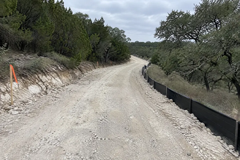 Road building permits in Texas: New limestone road through cedar with silt fence and flagged survey stakes