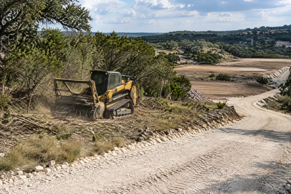 Development site clearing: track mulcher beside a crushed limestone entrance road and graded pads
