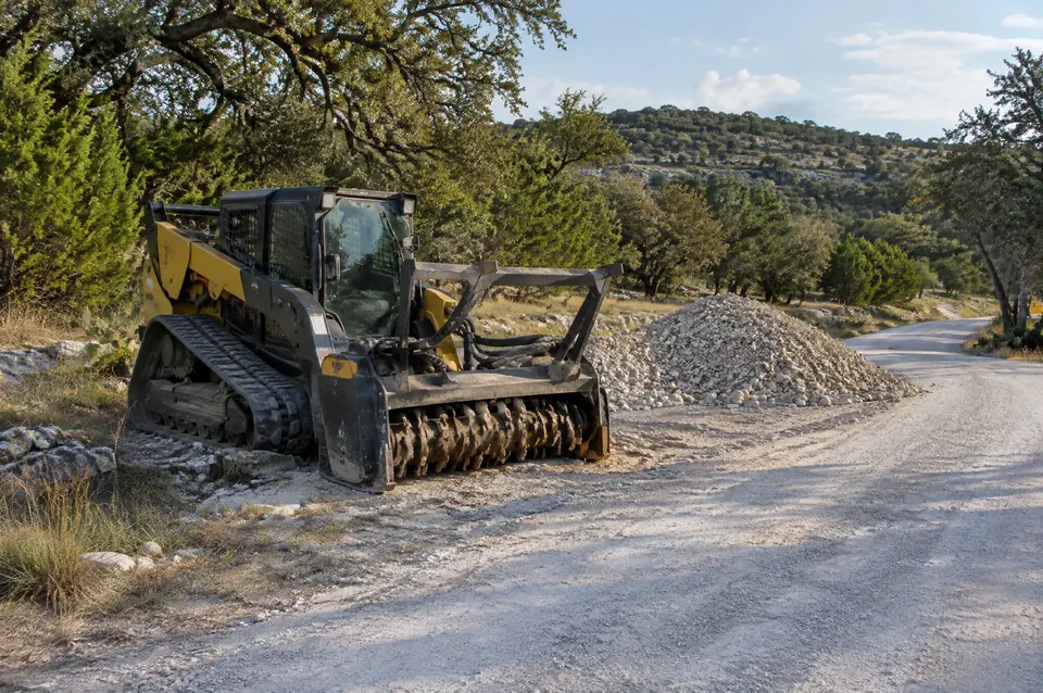 Hill Country land services: track mulcher beside a crushed limestone road and a pile of road base