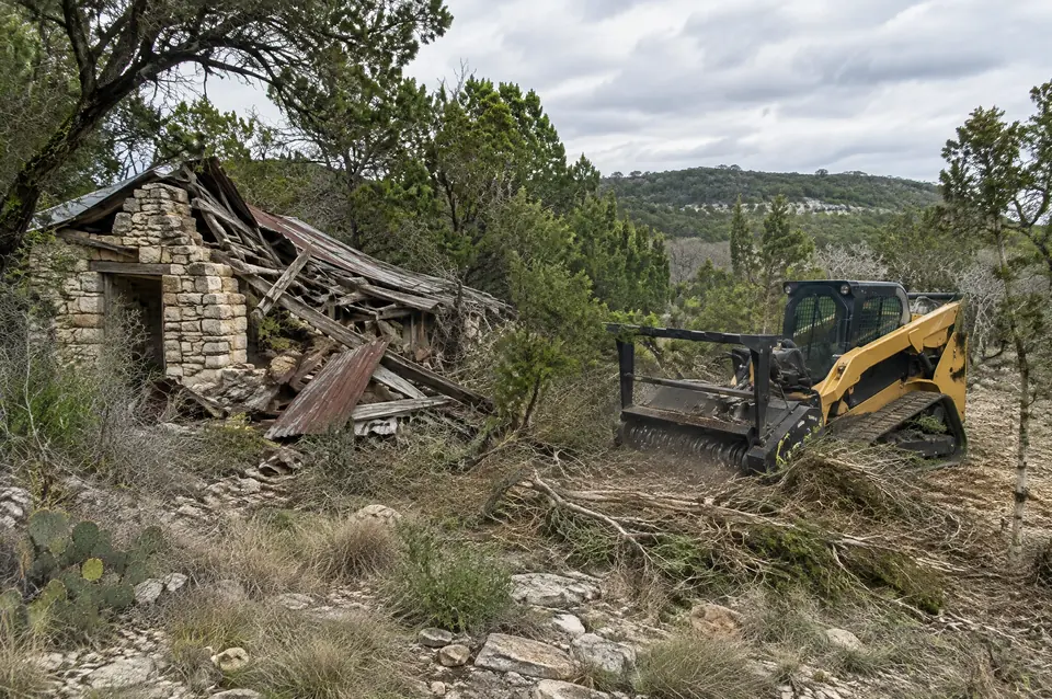 Building lot clearing New Braunfels: track mulcher clearing brush around an old collapsed stone shed near New Braunfels