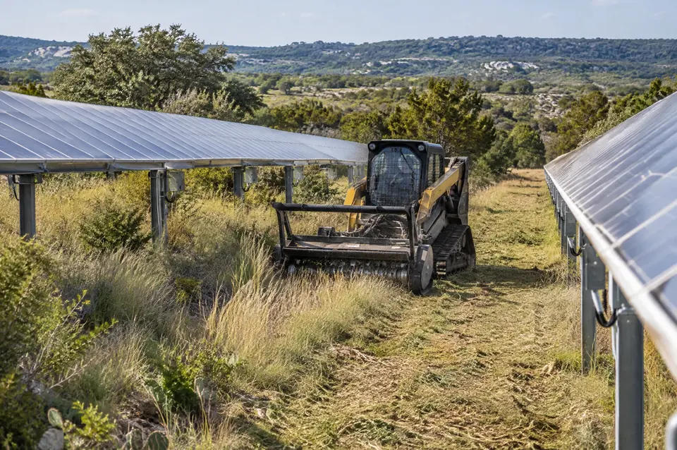 Mass acreage clearing: track mulcher cutting grass between rows of solar panels