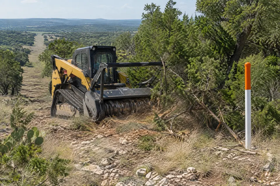 Pipeline right of way clearing: track mulcher cutting regrowth beside a pipeline marker post