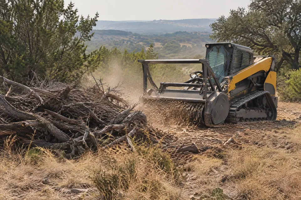 Comal County brush clearing: track mulcher grinding dry cedar brush piles on a Comal County pasture